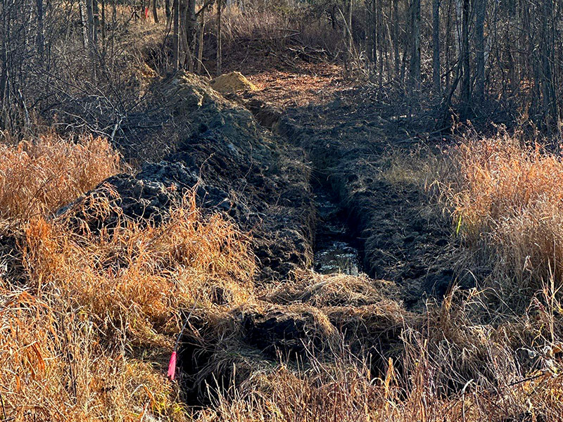 Underground service trench routed through wooded rural terrain