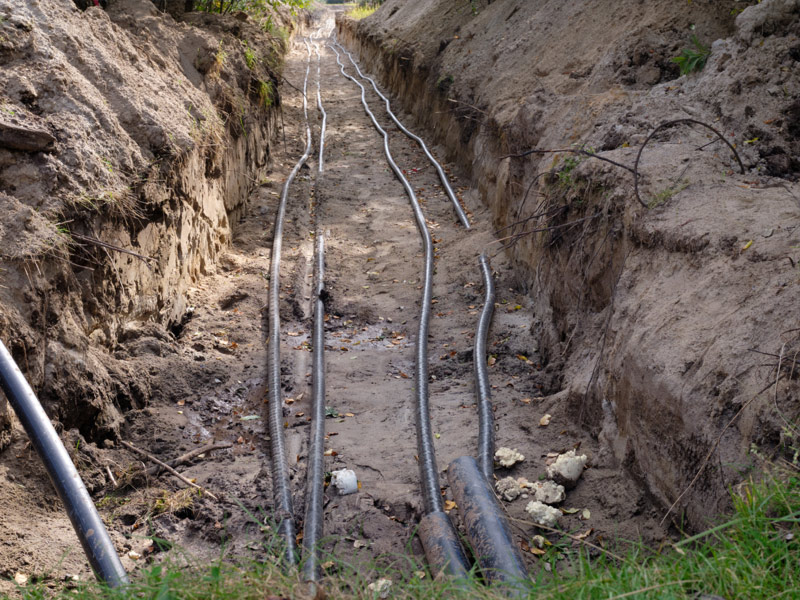 Multiple underground utility conduits laid in an open trench before backfilling.